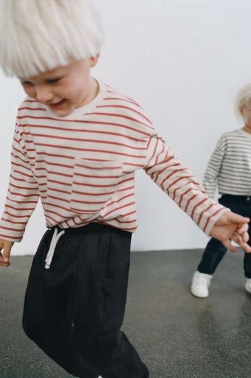 Child wearing striped long-sleeve shirt and dark pants laughing indoors