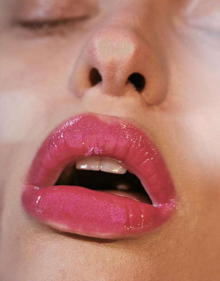 Close-up of a woman's face featuring pink, glossy lips, a visible nose, and closed eyes, highlighting beauty and skincare elements.