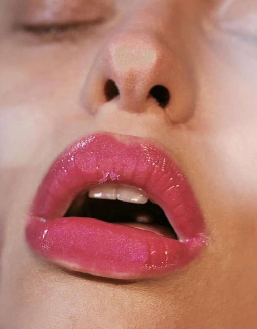 Close-up of a woman's face featuring pink, glossy lips, a visible nose, and closed eyes, highlighting beauty and skincare elements.