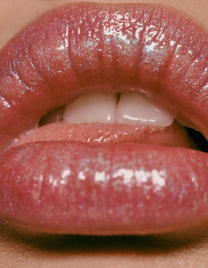 Close-up shot of a woman's glossy, pink lips slightly parted, revealing white teeth and a hint of her tongue. Beauty concept.