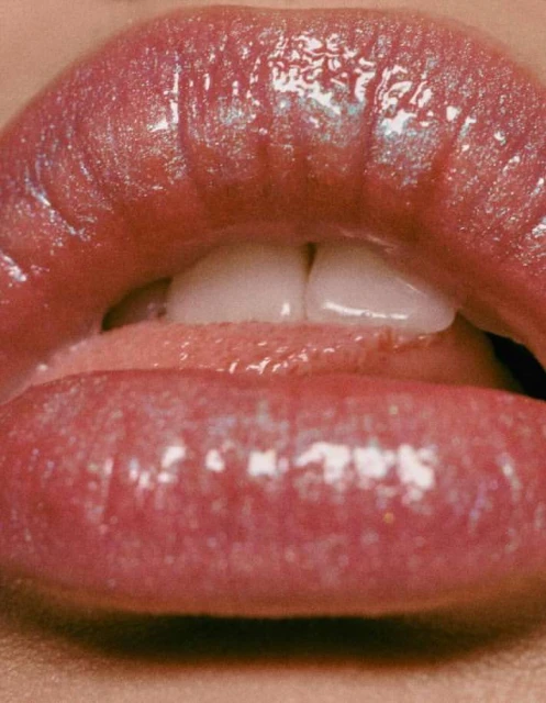 Close-up shot of a woman's glossy, pink lips slightly parted, revealing white teeth and a hint of her tongue. Beauty concept.