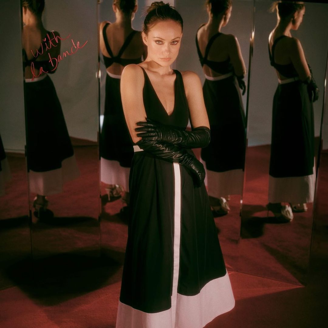 Fashion portrait of a woman wearing a sleeveless black and white dress and long black gloves, posing in front of mirrors.