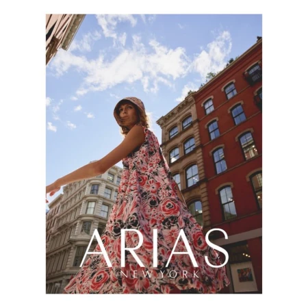 Adult woman in floral print dress and matching bucket hat walking in a city, buildings and blue sky in the background, low angle view.