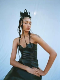 Portrait of a woman wearing a black leather dress with intricate braided updo and silver chain accessory against a white seamless background