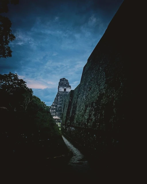 Low-angle view of a Mayan temple complex in Tikal National Park, Guatemala, at dusk, emphasizing the architectural details and dense forest setting.