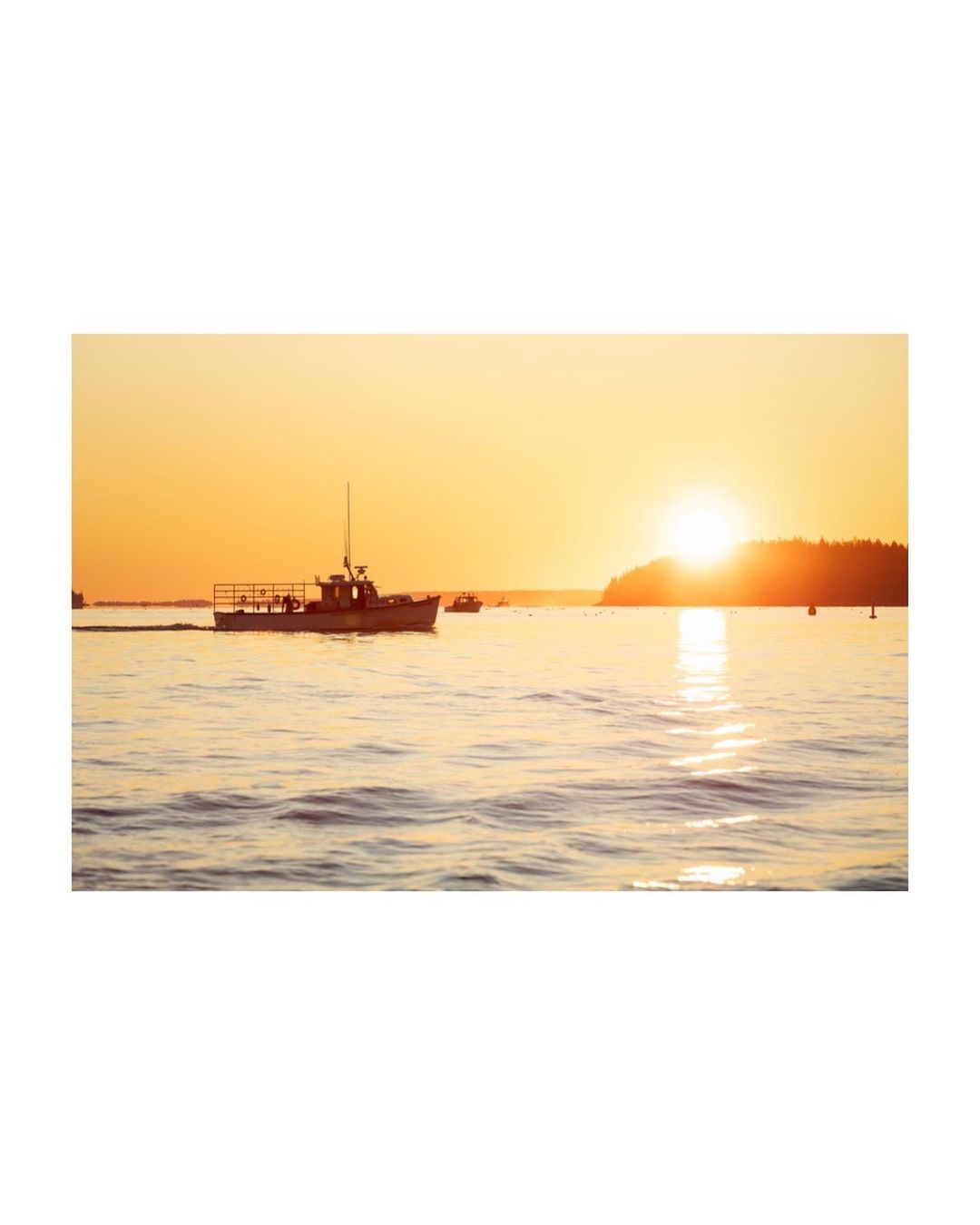 Scenic view of a boat on the water with the sun setting over a distant island, creating a warm, golden light.