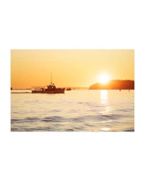 A fishing boat navigating calm coastal waters at sunset with a bright sun on the horizon.