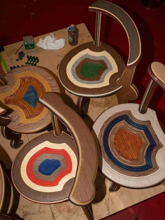 Handcrafted chairs featuring multi-layered wood designs, set against a rustic background. These chairs showcase unique, artisan craftsmanship.