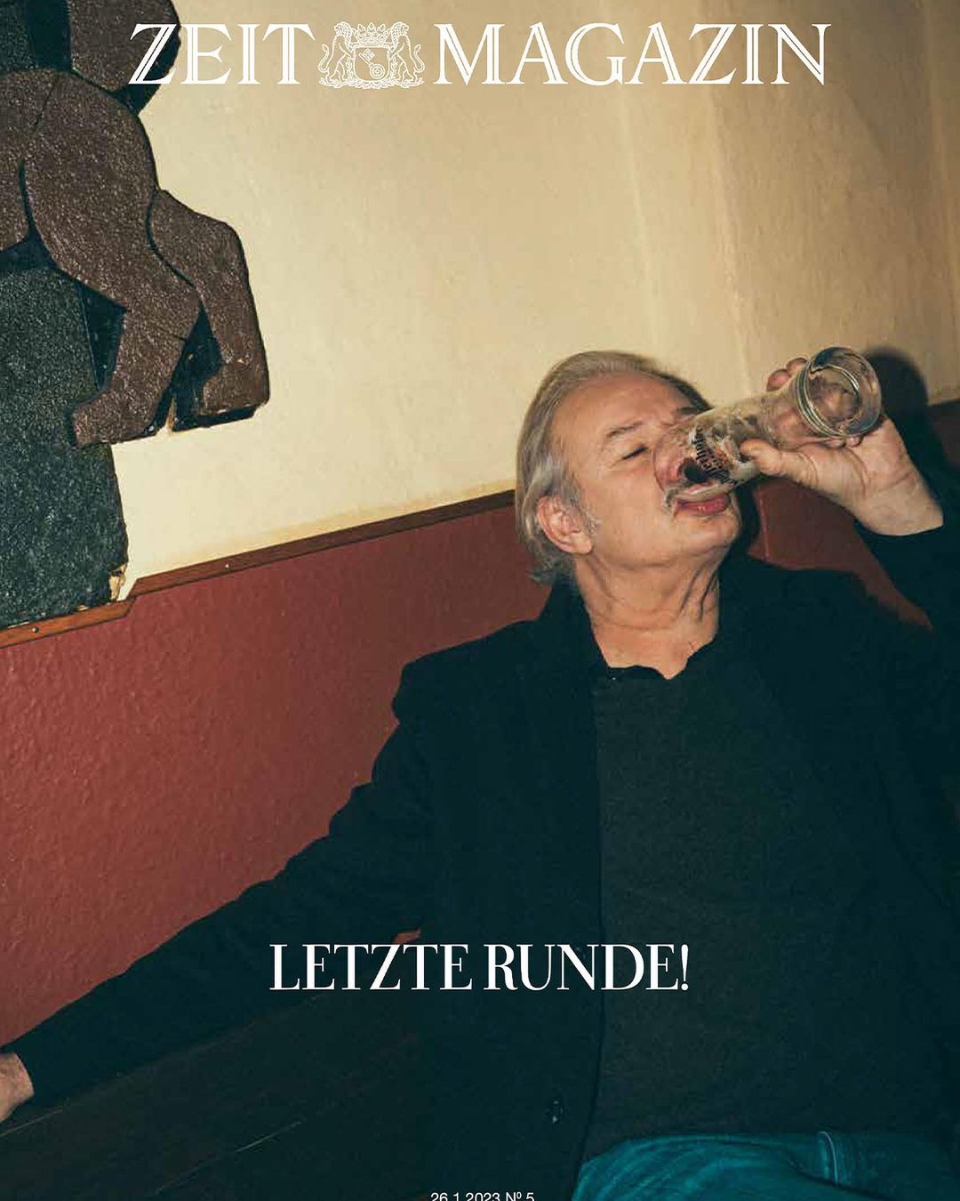 Zeit Magazin cover featuring a mature man drinking from a glass bottle indoors with a wooden sculpture in the background.