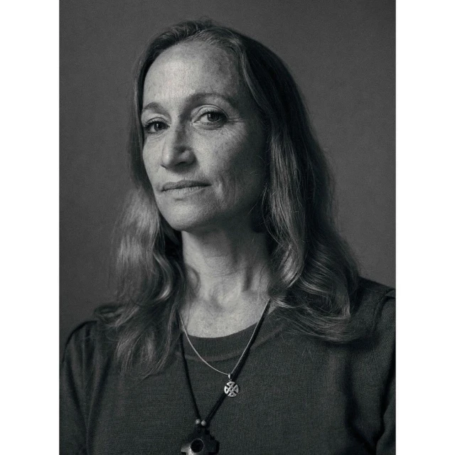 Monochrome portrait of an adult woman with long wavy hair, wearing a dark top and pendant necklaces against a plain background.
