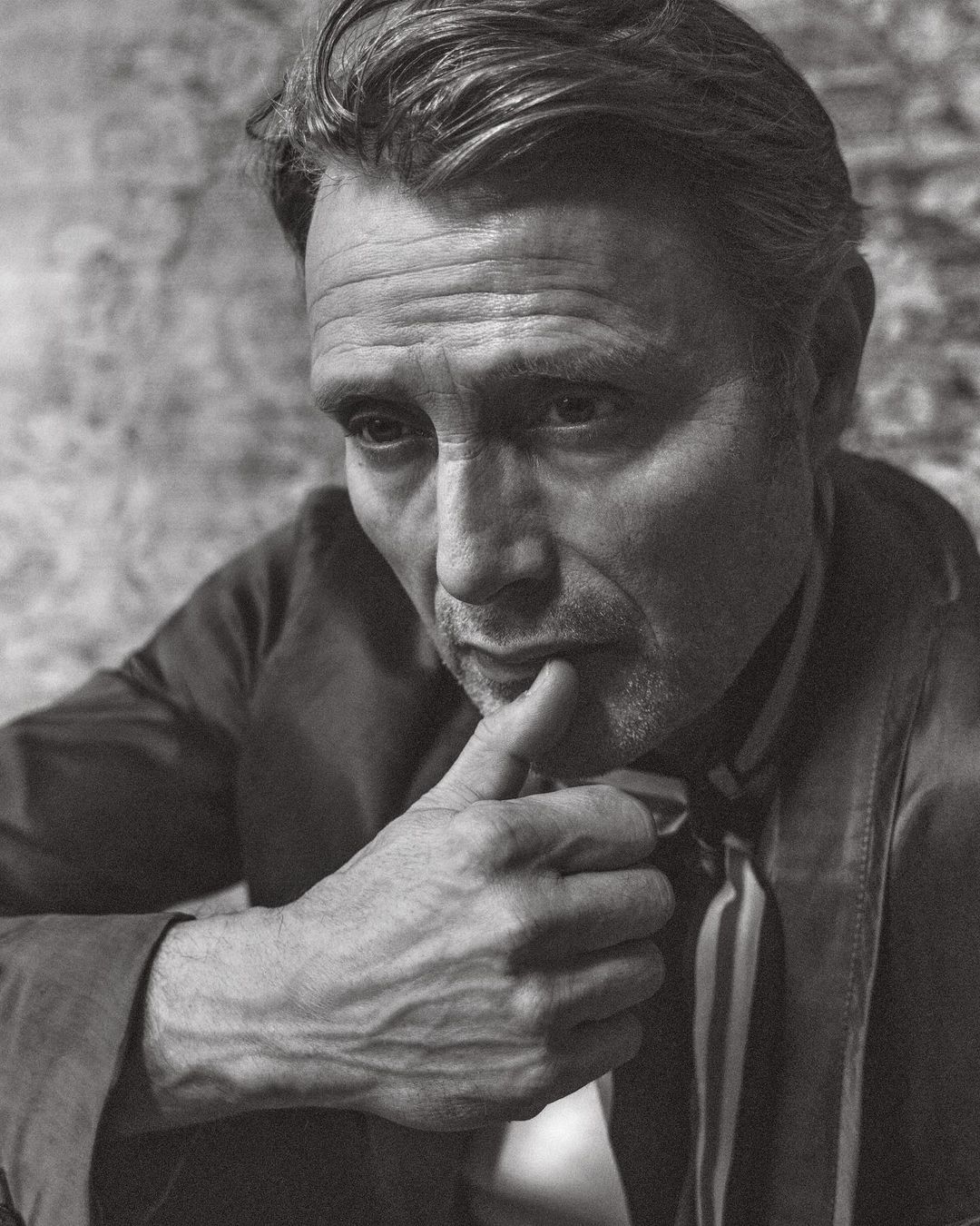 Portrait of an adult male with a neutral expression in a close-up shot against a textured background in black and white.
