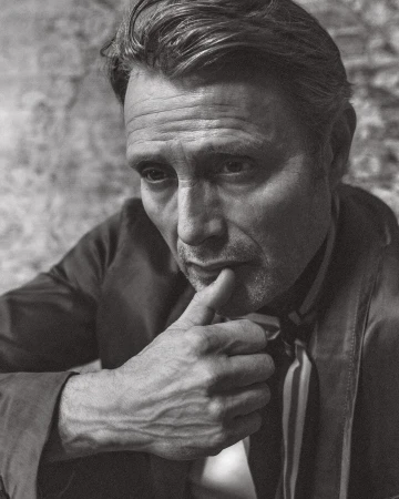 Portrait of an adult male with a neutral expression in a close-up shot against a textured background in black and white.