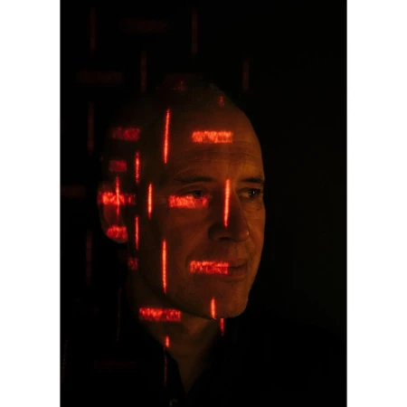Portrait of an adult man with fair skin and a bald head, with red digital grid patterns overlayed on his face in a studio setting.