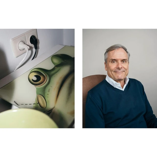 Indoor split shot: a man with short grey hair wearing a navy sweater smiles to the right of a frog illustration with an outlet.