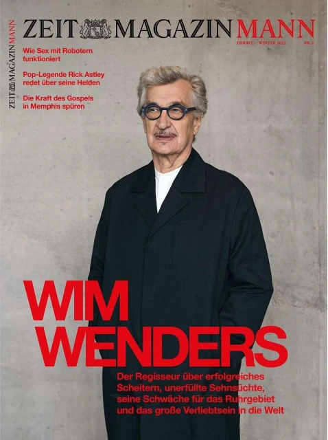 Magazine cover featuring an adult man with gray hair and glasses wearing a dark overcoat, with red text on a concrete-textured background.