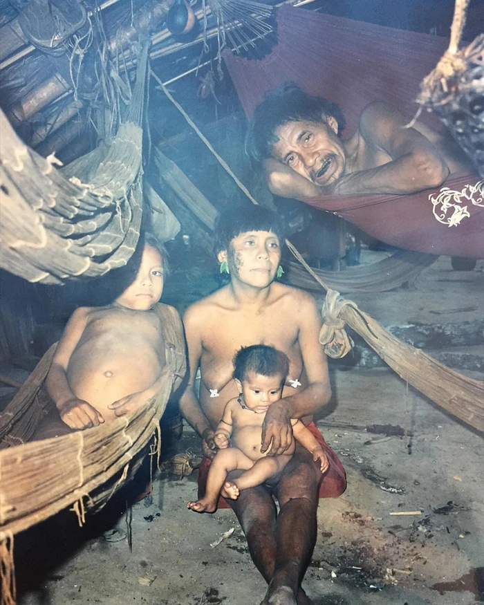 Indigenous family inside a rustic shelter with woven hammocks hanging overhead, photographed by Matthias Ziegler.