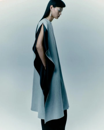 Fashion shot of an Asian female model in studio wearing a light grey cape with black lining, long black hair, and silver earrings.