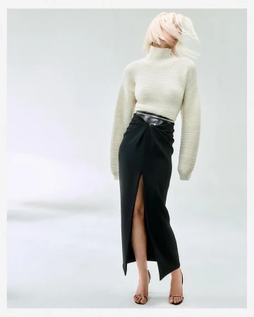 Model with blonde hair whipping across face, wearing ribbed white turtleneck and black slit skirt by Matthieu Delbreuve