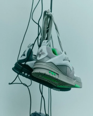 Grey sneakers hanging by laces from vertical wires against a neutral grey studio background