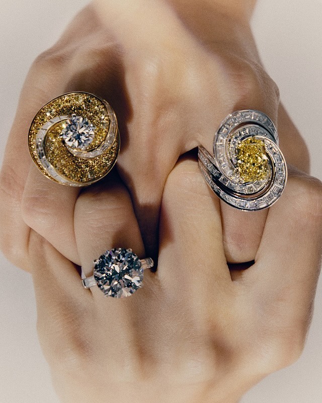 Hand showcases three diamond rings with different stone colors and settings. Jewelry shot for fashion, beauty, and luxury concepts.