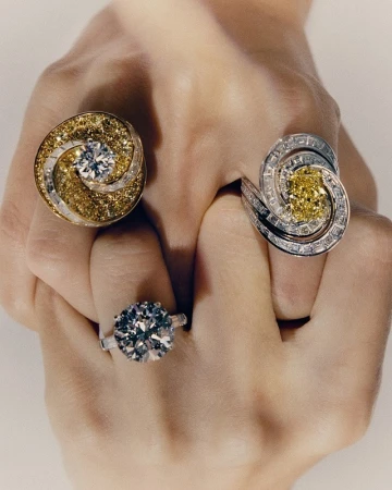 Hand showcases three diamond rings with different stone colors and settings. Jewelry shot for fashion, beauty, and luxury concepts.