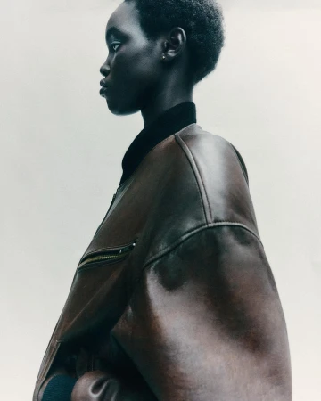Portrait of Black woman in leather jacket, side view against white backdrop, showcasing fashion and beauty in a minimalist setting.