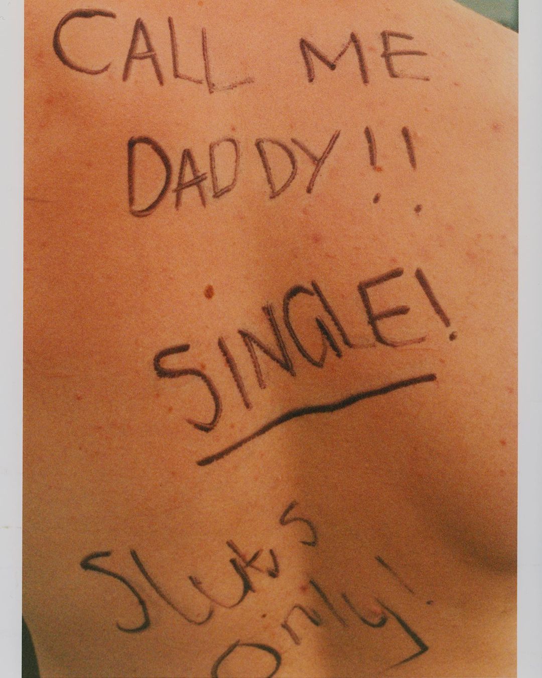 Close-up photo of bare human back with handwritten black marker text reading, "Call Me Daddy!! SINGLE! Sluts Only!"