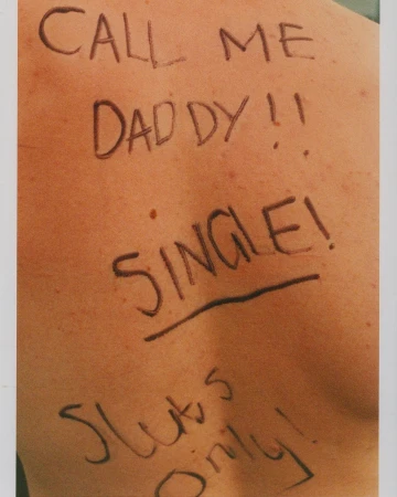 Close-up photo of bare human back with handwritten black marker text reading, "Call Me Daddy!! SINGLE! Sluts Only!"