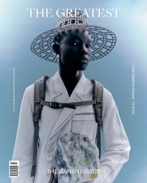 Magazine cover featuring a dark-skinned person wearing a wide-brimmed hat, backpack, and holding a rock against a pale blue background.