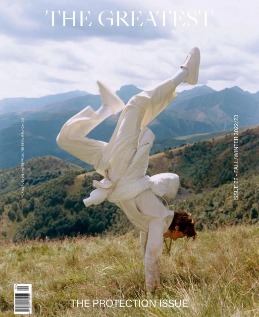 Magazine cover featuring a handstanding person in white clothing outdoors with a mountain range in the background under a cloudy sky.