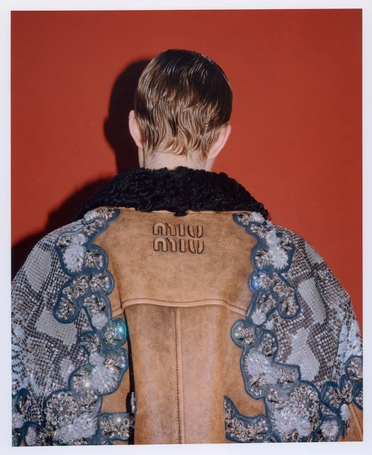 Person wearing a Miu Miu jacket with black fur collar against a red background, seen from the back.