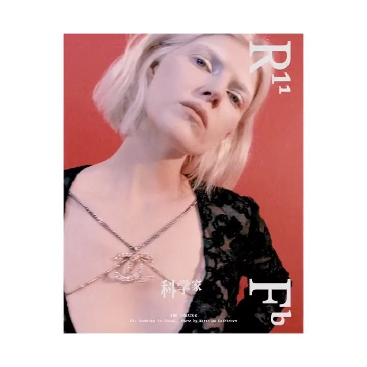 Fashion editorial shot of a fair-skinned woman with blonde hair, wearing a Chanel body chain against a red background with magazine text.