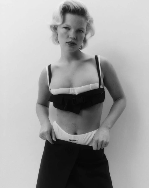 Blonde woman in black and white underwear-themed fashion, posing against a white background with neutral expression, fashion editorial style.