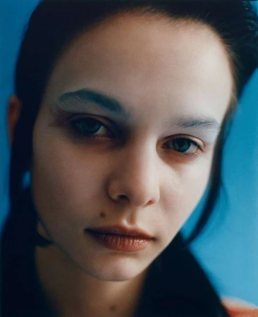 Close-up portrait of a young woman with pale blue eyeshadow against a solid blue background by Matthieu Delbreuve