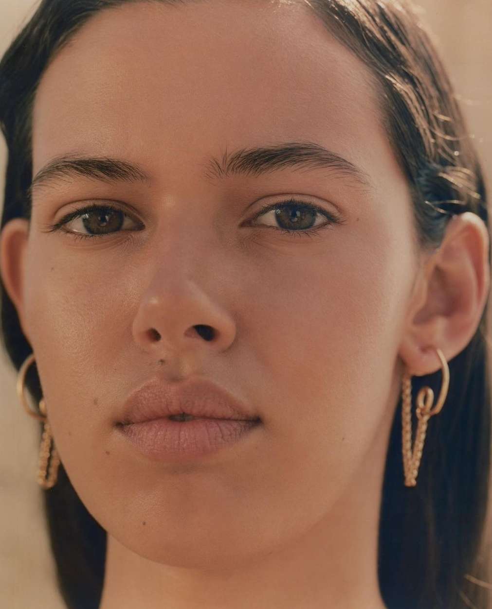 Close-up portrait of a woman with dark hair wearing gold hoop earrings by photographer Matthieu Delbreuve