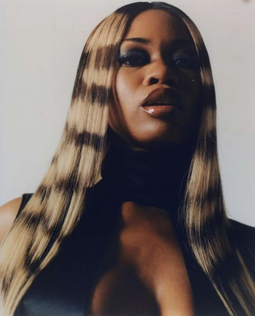 Glamorous portrait of an adult female with highlighted blonde hair and dark makeup in a black top against a plain white background.