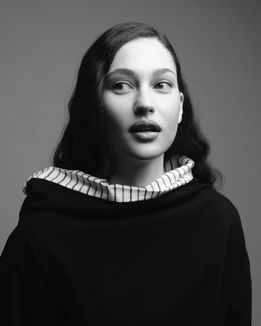 Portrait of a brunette adult female looking off-camera in black and white with soft studio lighting and dark clothing with striped trim.