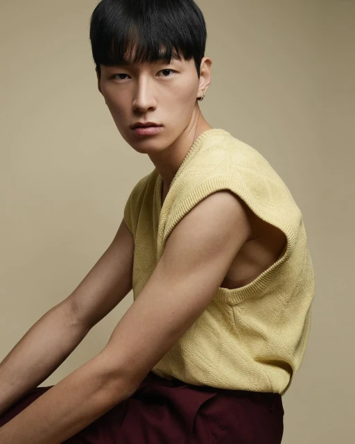 Portrait of a young adult Asian male wearing a yellow knit vest and maroon pants, posing in a studio with a neutral background.