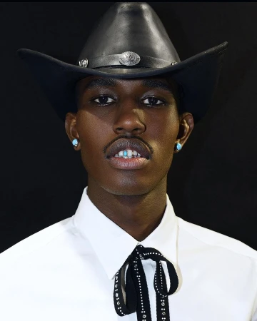 Close-up of a Black adult male wearing a cowboy hat, white shirt, and turquoise earrings against a dark background.