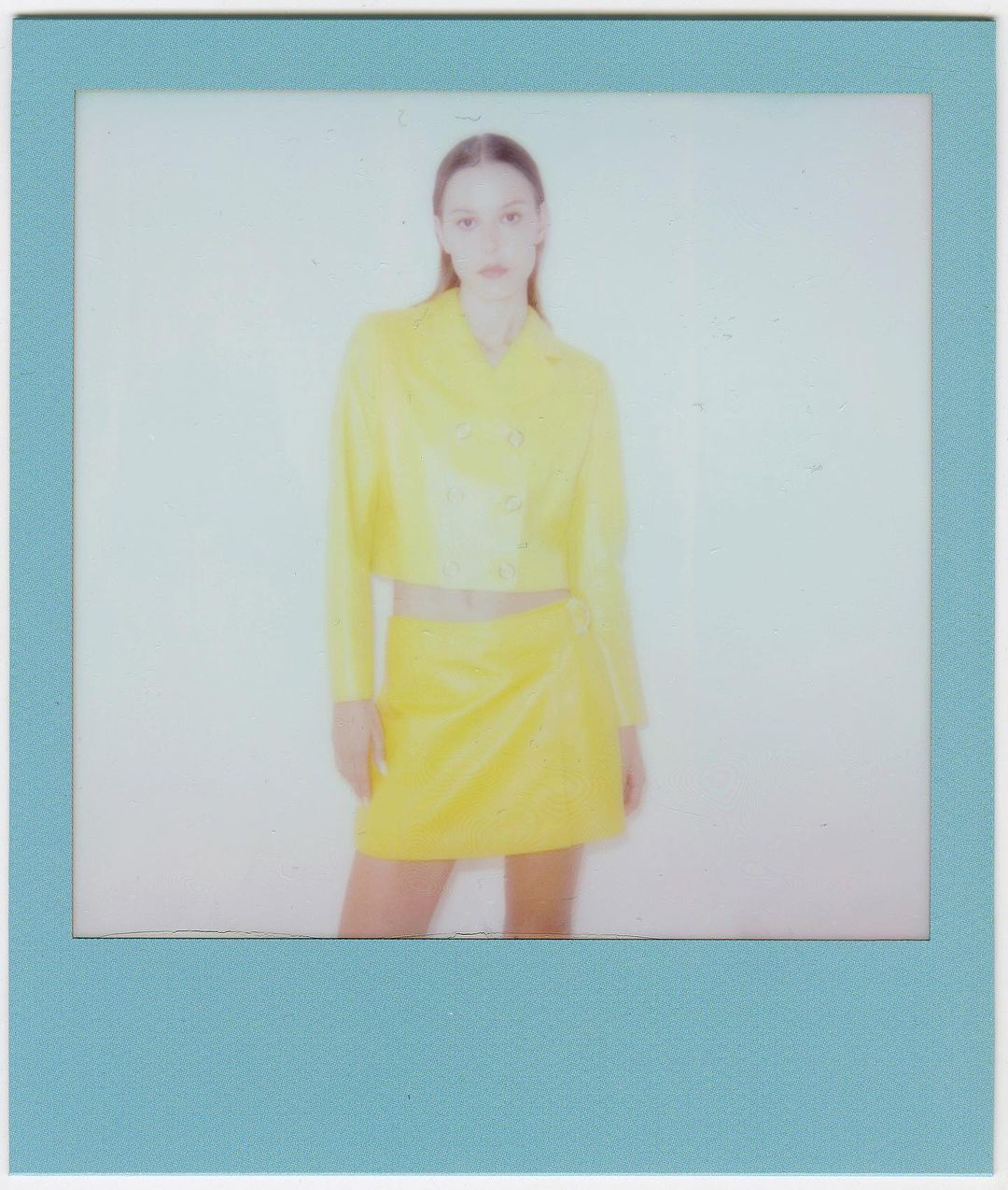 Woman in yellow outfit posing in photo-studio portrait with a blue frame. Fashion shot of stylish jacket and skirt with neutral backdrop.