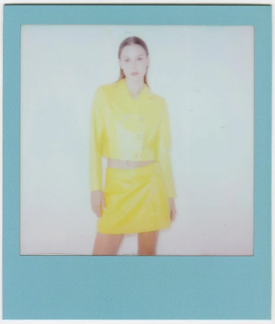 Woman in yellow outfit posing in photo-studio portrait with a blue frame. Fashion shot of stylish jacket and skirt with neutral backdrop.