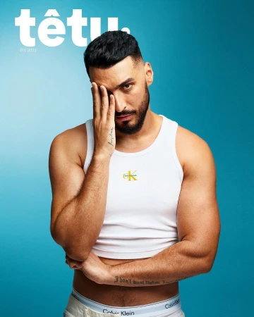 Man covering his eye with his hand wearing a white tank top against a bright blue background