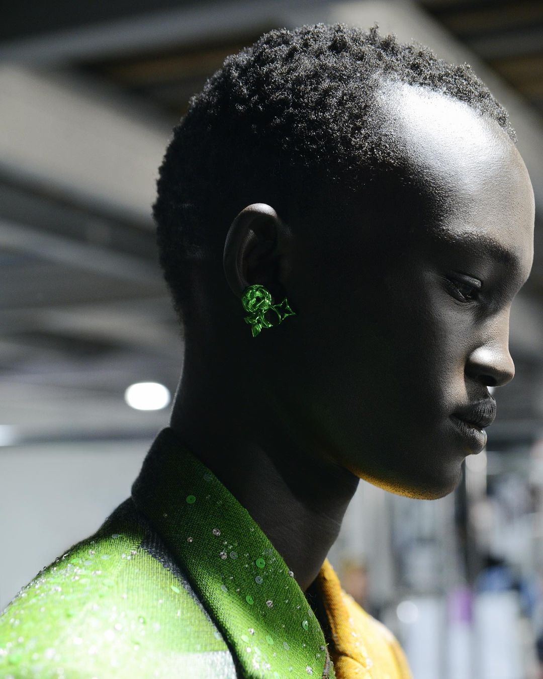 Close-up of a Black adult female model wearing a lime-green jacket and green earrings in a studio. Beauty and fashion shot.