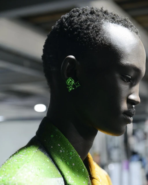 Close-up of a Black adult female model wearing a lime-green jacket and green earrings in a studio. Beauty and fashion shot.