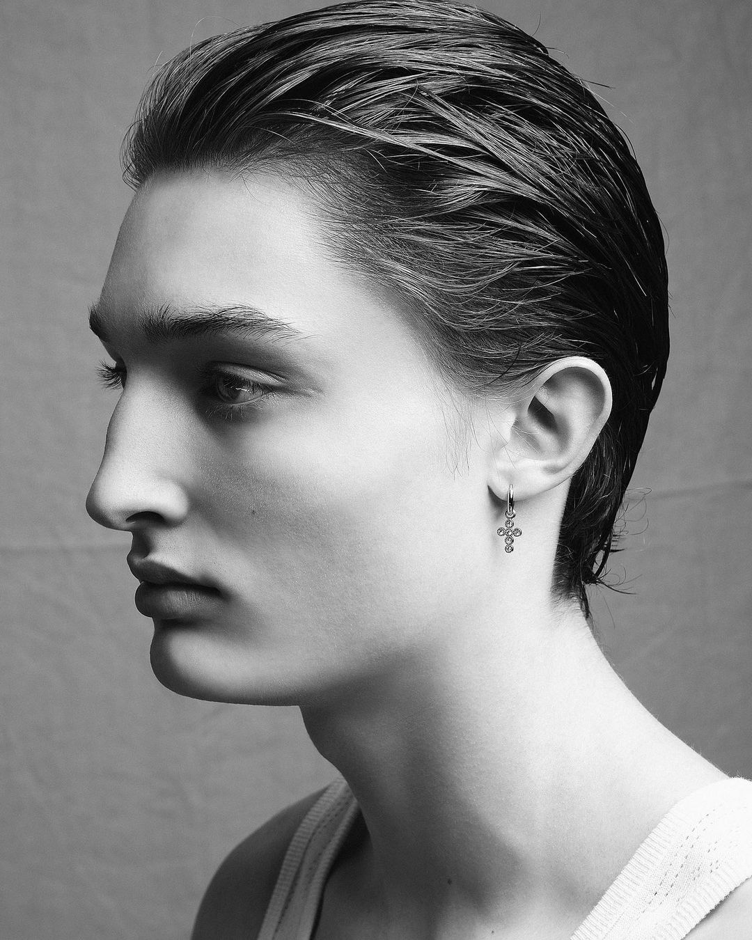 Monochrome portrait of a young adult male with slicked-back hair, wearing an earring, against a neutral backdrop in soft lighting.