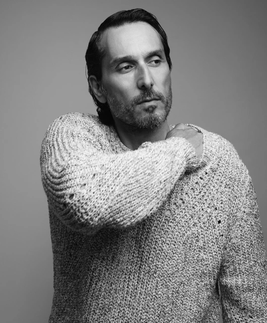 Black and white portrait of a mature adult male in a knit sweater, posing in a photo studio. The man is looking off to the side.