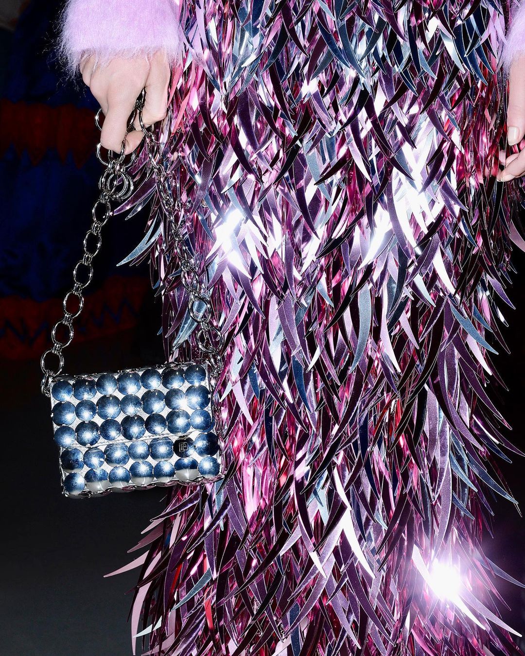 Close-up of a person in a shimmering pink dress holding a silver beaded handbag with a chain strap. Fashionable and eye-catching.