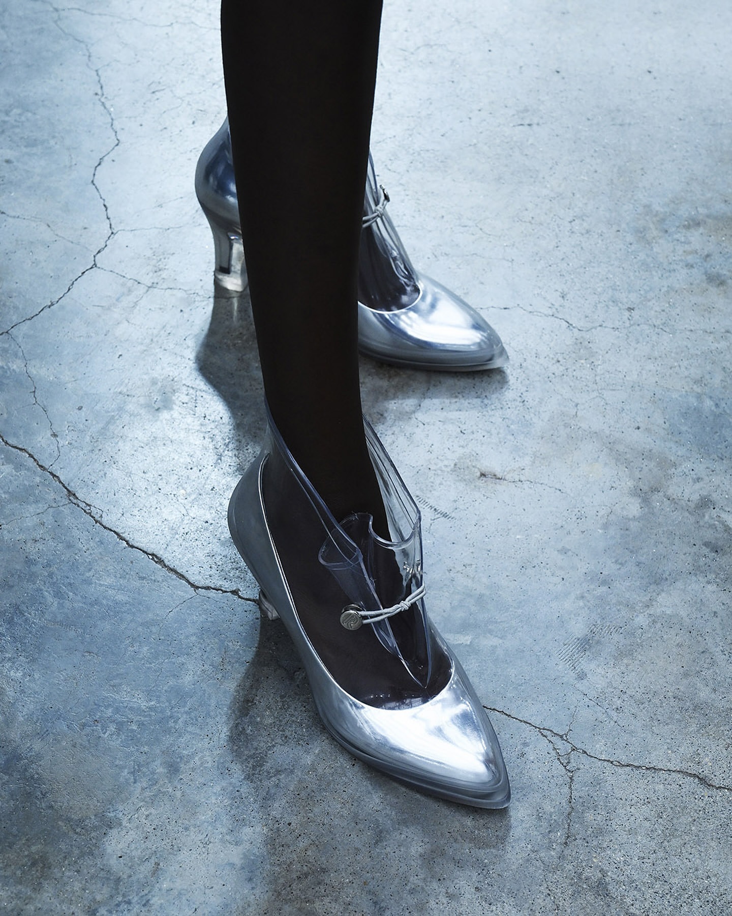 Close-up of silver high heels with a clear top on a woman's feet, posing on a concrete floor. Fashionable footwear with an elegant design.