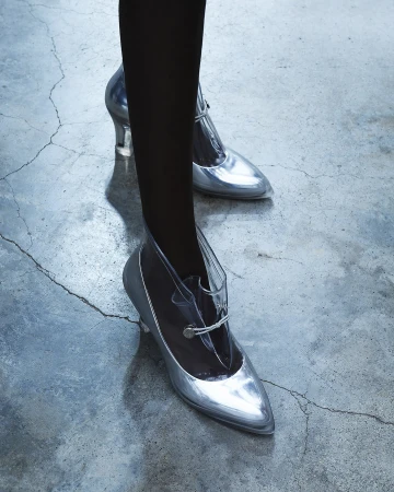 Close-up of silver high heels with a clear top on a woman's feet, posing on a concrete floor. Fashionable footwear with an elegant design.