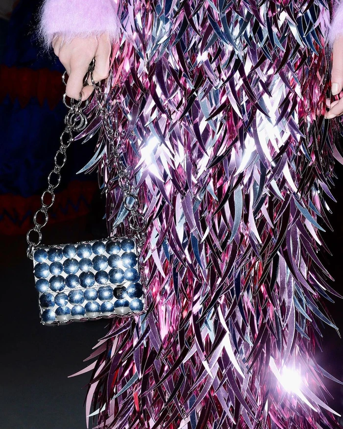 Close-up of a person wearing a shimmering metallic fringed garment and holding a studded silver shoulder bag with chain strap.
